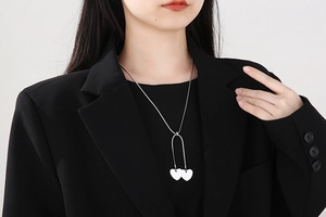 Detail of silver heart pendants on a sleek snake chain necklace worn by a model