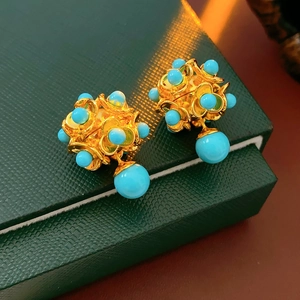 Détail de boucles d'oreilles fleurs dorées vintage avec perles turquoise sur écrin