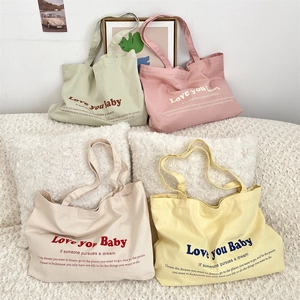Detail of four colorful canvas tote bags with 'Love you Baby' print on a soft white sofa