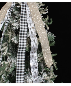 Close-up of festive plaid and tree print ribbons hanging on a snowy Christmas tree branch