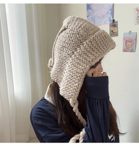 Détail du bonnet à oreillettes en grosse maille beige avec pompons et tresses larges
