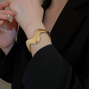 Polished gold wave open cuff bracelet shown on wrist with a minimalist design