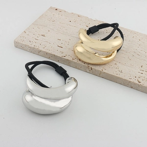 Close-up of sleek gold and silver metal chain hair ties on a travertine display stand