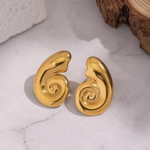 Detail of golden spiral shell earrings on minimalist stone and wood background