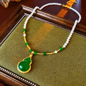 Détail du pendentif gourde verte et des perles sur fond de tissu vert vintage