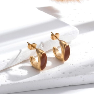 Boucles d'oreilles C dorées minimalistes avec émail marron sur un support texturé