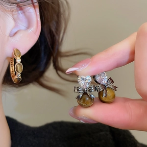 Detail of gold-plated tiger eye earrings with heart zircon and vintage bow accents
