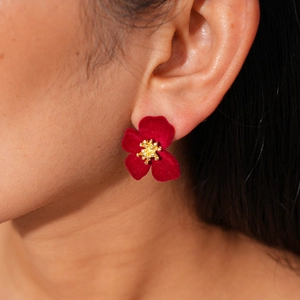 Gros plan d'une boucle d'oreille fleur rouge velours avec centre doré sur l'oreille