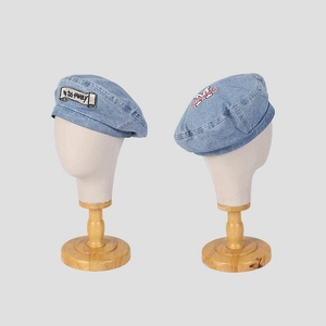 Washed light blue denim beret with vintage patch and embroidery on a white display head