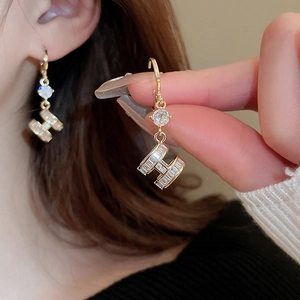 Close-up of gold-plated H letter drop earrings with inlaid sparkling crystals