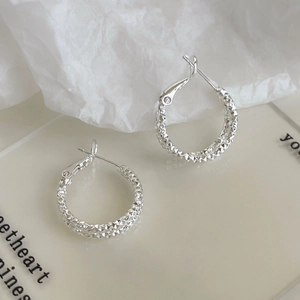 Macro detail of silver geometric hoop earrings with textured diamond-cut surface pattern