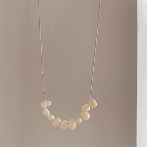 Detail of silver chain with U-shaped baroque pearls over a clean beige backdrop