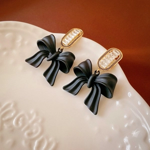 Macro detail of black velvet bow earrings with rectangular zircon studs on ceramic plate
