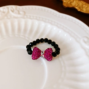 Close-up of handmade black beaded ring with a pink rhinestone bow and iridescent center