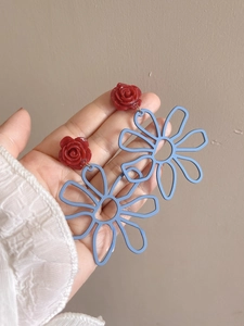 Detail of hollow floral earrings with red resin rose and blue contrast petals