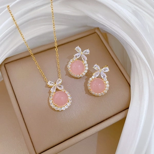 Titanium steel bow jewelry set with pink stones on a beige display cushion