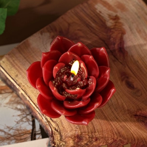 Macro detail of red succulent flower candle with a lit wick on dark wood background