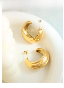 Detail of gold textured C-shape hoop earrings with grooved patterns on a white plate