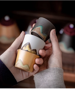 Close-up of three ceramic Japanese style teacups with landscape pattern held in hand