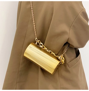 Detail of a gold cylindrical evening bag with metal chain strap and luxury finish
