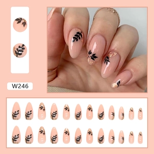 Detail of almond press-on nails with black leaf patterns and gold foil on pink base