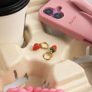 Detail of strawberry charm earrings in 18K gold stainless steel on a beige textured tray