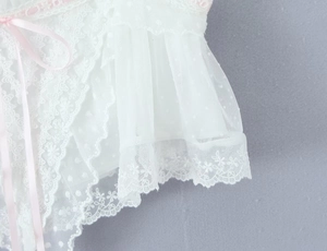 Detail aus weißem Spitzennetz mit Punkten und dezentem rosa Schleifenakzent