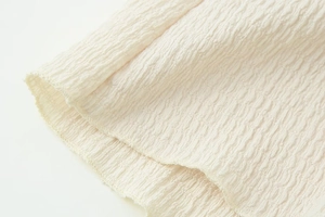 Detailed close-up of textured beige wavy fabric on a V-neck long sleeve top