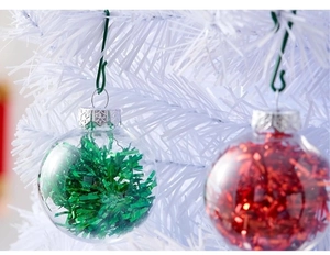 Close-up of clear PET Christmas ornaments with red and green tinsel on a white tree
