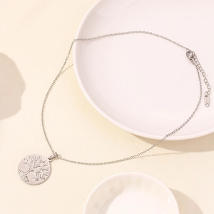 Macro detail of silver stainless steel tree of life pendant on a white ceramic plate