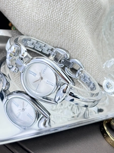 Macro detail of silver horsebit chain watch with oval dial on reflective tray