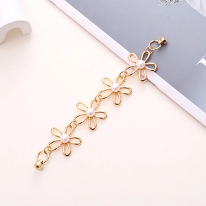 Detail view of golden flower chain with pearls and magnetic screw clasps on a beige surface