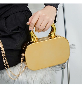 Detail shot of a golden acrylic mirror box bag with metallic chain held by a model