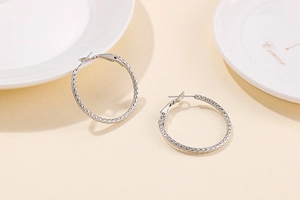 Detailed view of silver hoop earrings with intricate diamond pattern on beige background