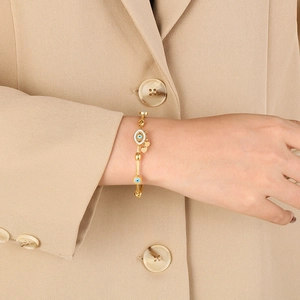 Gold Evil Eye bracelet with heart charm and blue drip oil detail on female model's wrist
