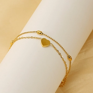 Close-up of double-layer gold anklet with heart pendant and beaded chain detail