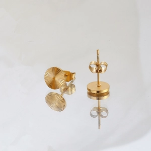 Detailed view of gold geometric sunburst earrings with a butterfly back on white mirror
