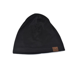 Detail of black knit beanie with brown leather F&S logo patch on soft cotton fabric