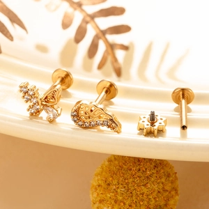Detailed view of golden butterfly and flower ear studs set with sparkling zircons on ceramic