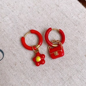 Close-up of asymmetric stainless steel earrings with red flower and mini handbag charm