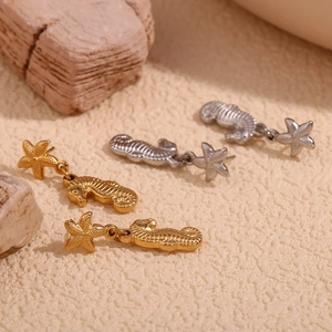 Detail of 18K gold and silver seahorse and starfish earrings on textured stone surface