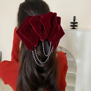 Detail view of oversized red velvet bow hair clip with elegant hanging pearl chains