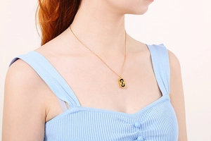 Detail of paperclip chain necklace featuring a two-tone oval hollow pendant on a model