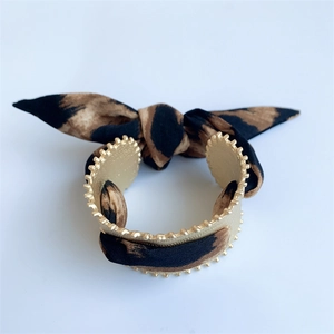 Close-up of leopard print silk scarf ribbon tied on a matte gold gear-edge cuff bracelet