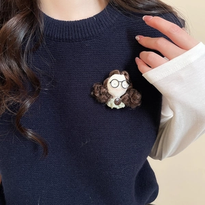 Detailed view of a handmade cartoon girl brooch pinned on a navy blue knit sweater