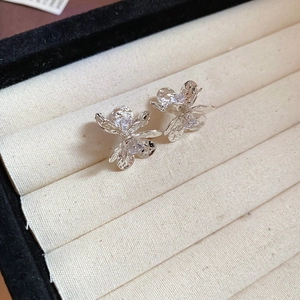 Close-up of silver flower stud earrings with zircon inlay on beige cotton cushion