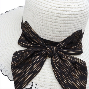 White lace straw sun hat for women featuring a large black bow with gold metallic stripes