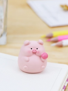 Close-up of a cute pink pig ornament holding a peach on a white notebook desk