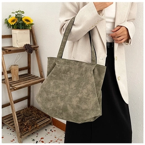 Detail of green suede tote bag with long handles shown in a lifestyle setting