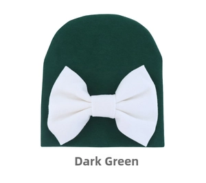 Detail view of dark green knitted baby hat featuring a large soft white bow design